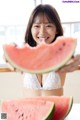 A woman in a white bra holding a slice of watermelon.