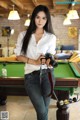 A woman holding a camera standing next to a pool table.