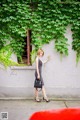 A woman standing in front of a wall covered in ivy.